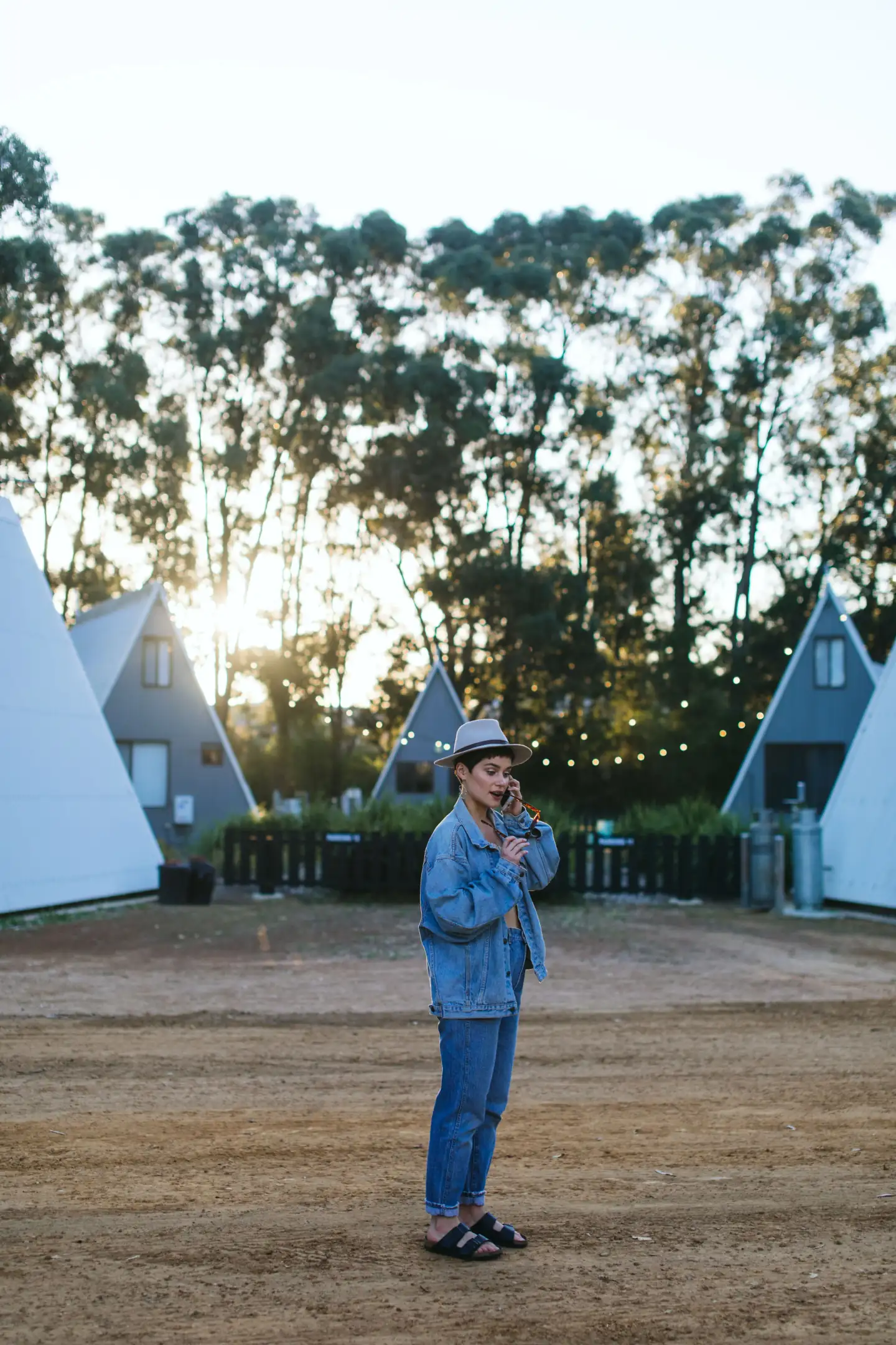 A traveler on the phone in front of A-frame cabins at dusk