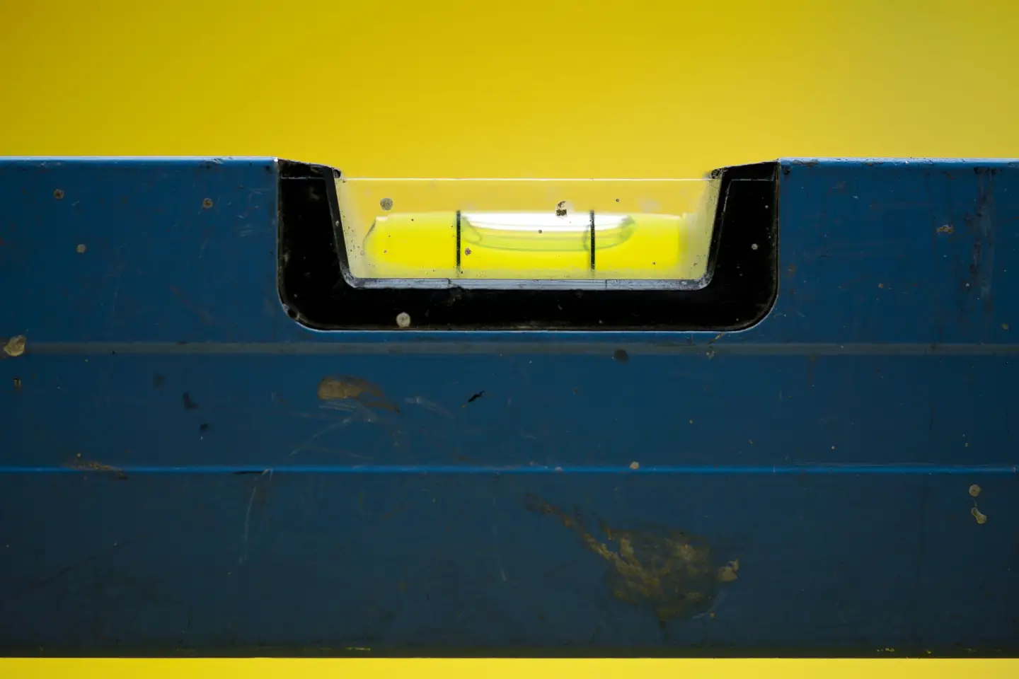 Close-up of a spirit level bubble resting at center against a yellow backdrop